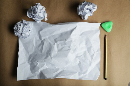 Crumpled up papers with a sheet of blank paper and a pencil on brown backgroundの写真素材