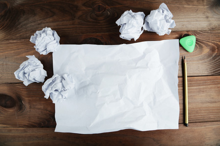Crumpled up papers with a sheet of blank paper and a pencil on brown wooden backgroundの写真素材