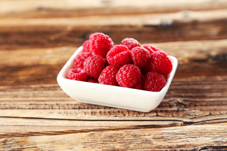 Raspberries in bowl on brown wooden backgroundの写真素材