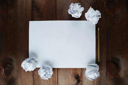 Crumpled up papers with a sheet of blank paper and a pencil on brown wooden backgroundの写真素材