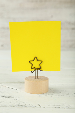 Yellow note paper on a holder on white wooden backgroundの写真素材