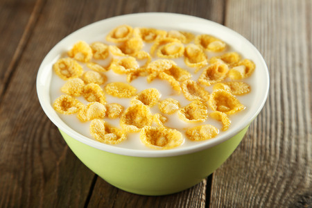 Bowl of cornflakes with milk on brown wooden background