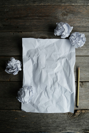 Crumpled up papers with a sheet of blank paper and a pencil on grey wooden backgroundの写真素材