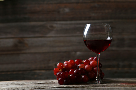 Glass of red wine with grapes on grey wooden background