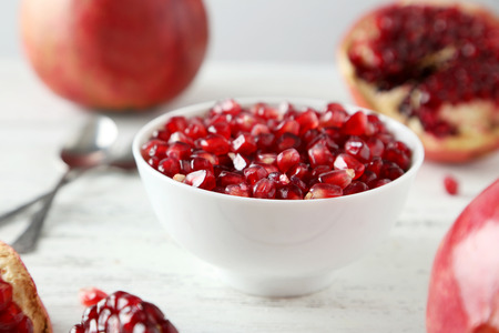 Delicious pomegranate fruit in bowl on white wooden backgroundの写真素材