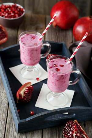 Pomegranate smoothie in glass and in tray on grey wooden backgroundの写真素材