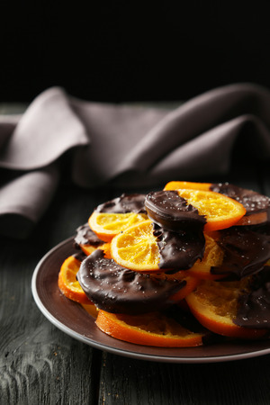 Delicious slices of orange coated chocolate on plate on black wooden backgroundの写真素材