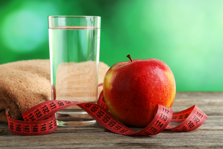 Red apple with measuring tape and glass of water on grey wooden backgroundの写真素材
