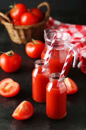 Fresh red tomatos and juice in bottles and jug on black backgroundの写真素材