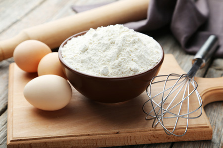 Bowl of wheat flour with eggs and whisk on grey wooden backgroundの写真素材