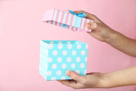 Female hands opening gift box on pink background