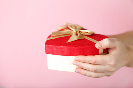 Female hands holding gift box on pink backgroundの写真素材