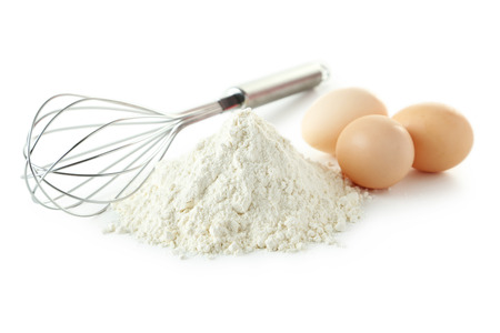 Heap of wheat flour with eggs and whisk isolated on whiteの写真素材