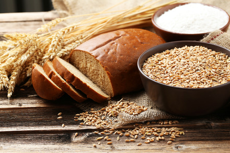 Ears of wheat and bowl of flour and wheat grains on brown wooden backgroundの写真素材