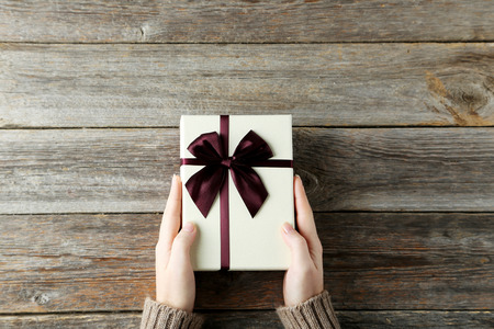 Female hands holding gift box on grey wooden backgroundの写真素材
