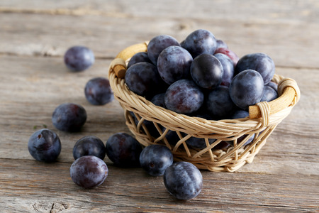 Fresh plums in basket on brown wooden backgroundの写真素材