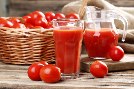 Fresh red tomatoes and tomato juice in glass on wooden tableの写真素材