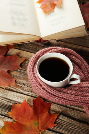 Cup of coffee with autumn leaves and a warm scarf on brown wooden backgroundの写真素材