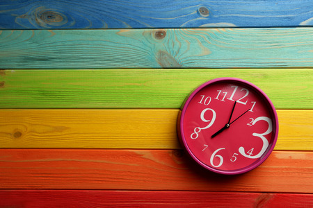 Pink round clock on a colorful wooden tableの写真素材