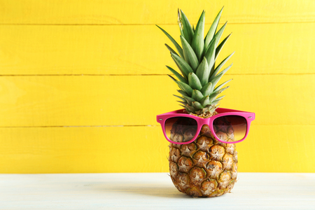 Ripe pineapple with sunglasses on a white wooden tableの写真素材