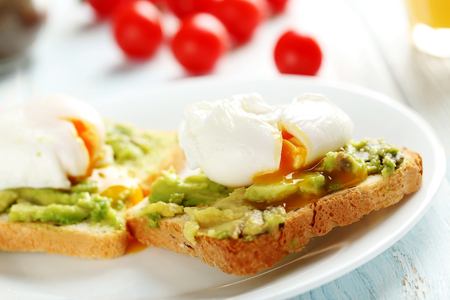 Poached eggs with avocado on toasts on blue wooden tableの写真素材