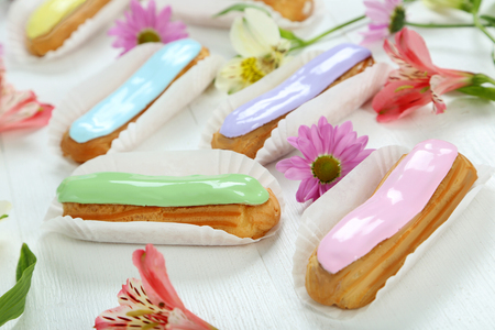 Eclairs with glaze on a white wooden table