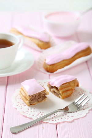 Eclairs with glaze on a pink wooden table