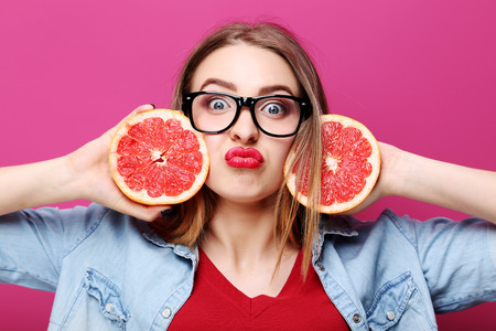 Portrait of a beautiful hipster girl with grapefruit on pink background