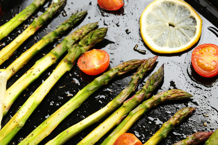 Fresh baked asparagus with lemons and tomatoes on black panの写真素材