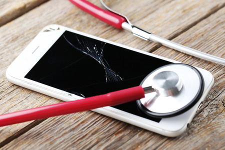 Broken smartphone with stethoscope on a grey wooden tableの写真素材