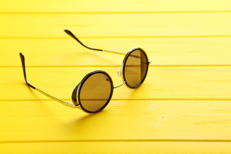 Black sunglasses on a yellow wooden tableの写真素材