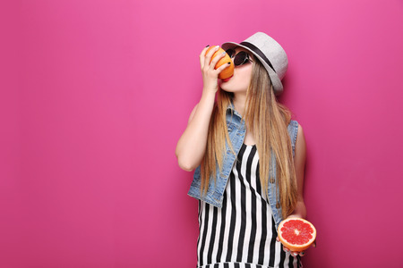 Portrait of a beautiful hipster girl with grapefruit on pink backgroundの写真素材