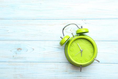 Green alarm clock on a blue wooden tableの写真素材