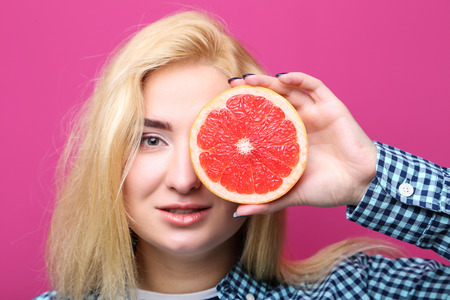 Young beautiful woman with grapefruit on pink backgroundの写真素材