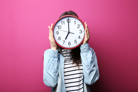 Young woman holding a clock on pink backgroundの写真素材