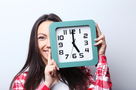 Young woman holding a clock on grey background