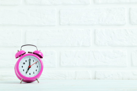 Pink alarm clock on the brick wall background