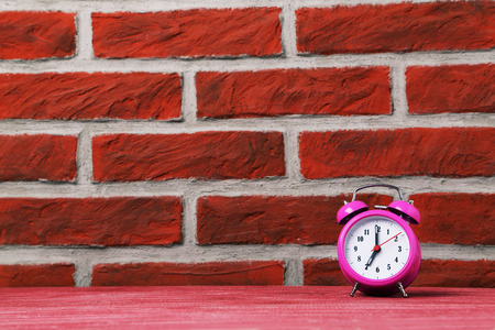 Pink alarm clock on the brick wall background