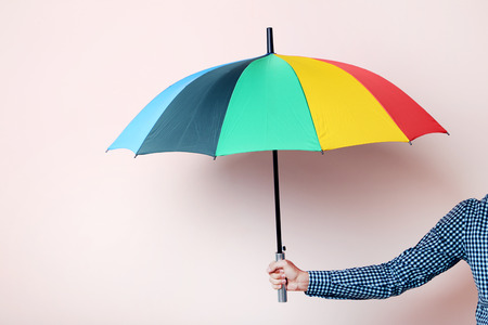 Colorful umbrella in male hand on beige backgroundの写真素材