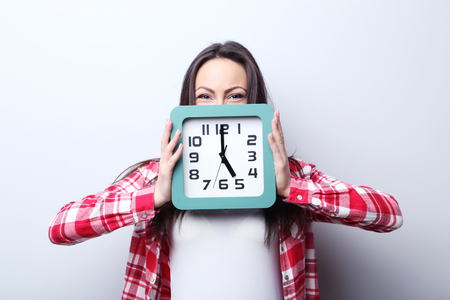 Young woman holding a clock on grey backgroundの写真素材