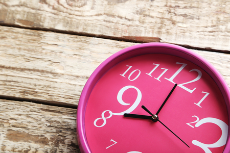 Pink round clock on a grey wooden table