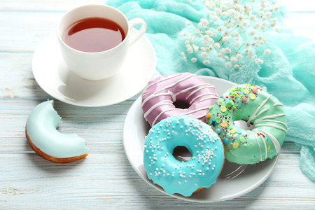 Tasty donuts with sprinkles and cup of tea on wooden tableの写真素材