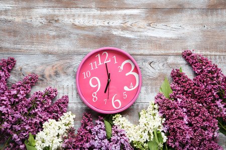 Branch of lilac flowers with round clock on wooden table