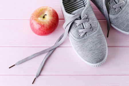 Grey sneakers with apple on pink wooden tableの写真素材