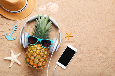 Ripe pineapple with sunglasses and headphones on beach sandの写真素材