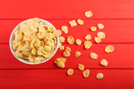 Cornflakes in bowl on red wooden table