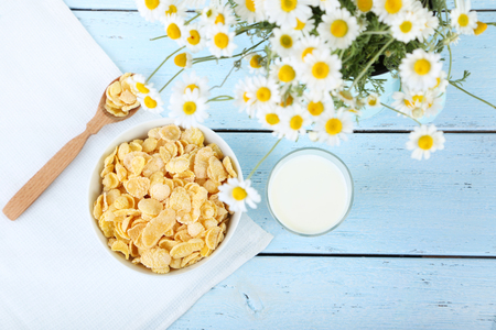 Cornflakes in bowl with glass of milk and chamomile on blue wooden tableの写真素材