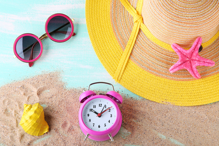Pink alarm clock with beach hat and sunglasses on blue wooden tableの写真素材