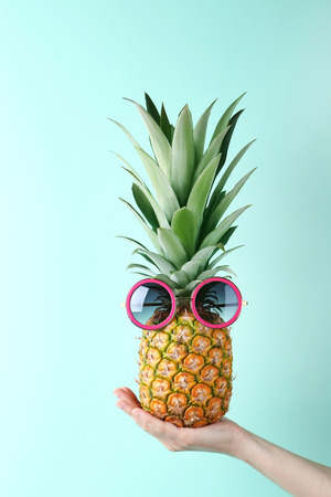 Female hand holding ripe pineapple with sunglasses on mint backgroundの写真素材
