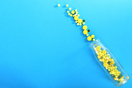 Yellow pills in glass bottle on blue backgroundの写真素材
